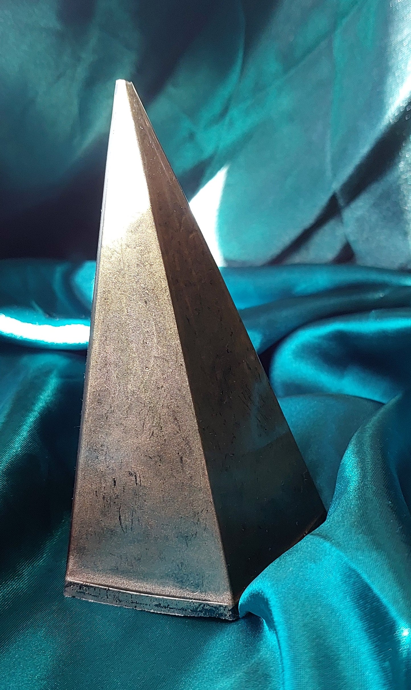 Metallic pyramid-shaped object on a teal fabric background